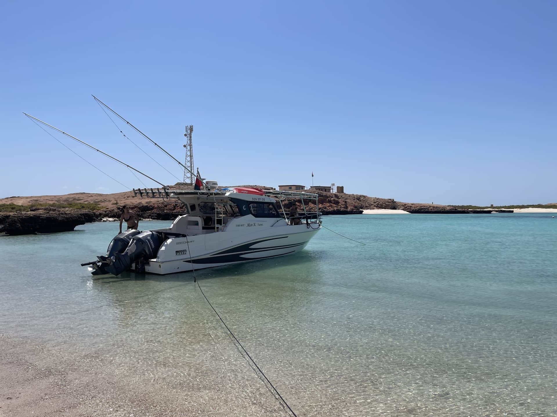 A Royal Marine Tours boat on calm turquoise water off the Muscat coast, ready for a fishing trip