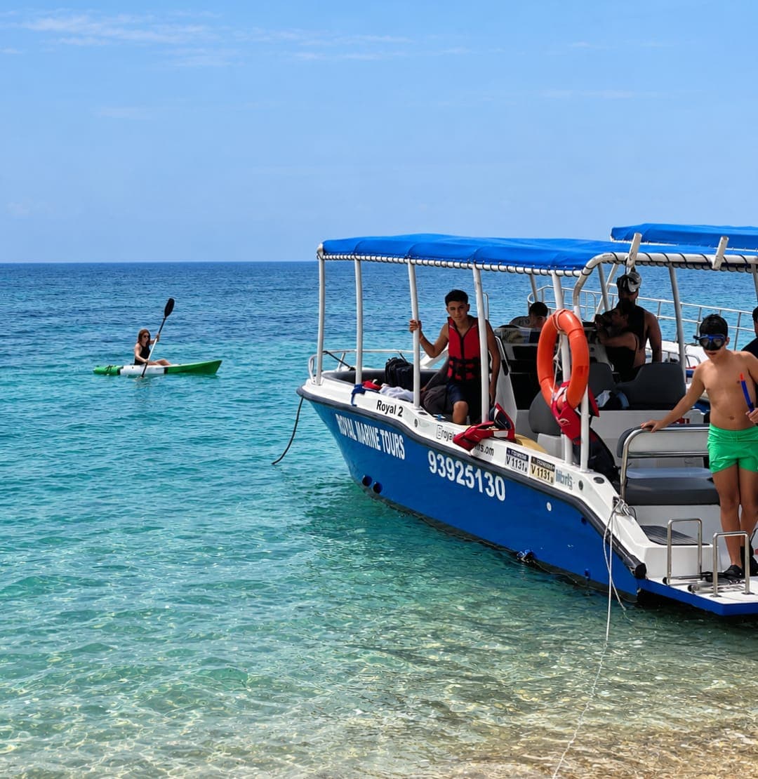A Royal Marine Tours boat with guests and a kayaker in turquoise water at the Daymaniyat Islands