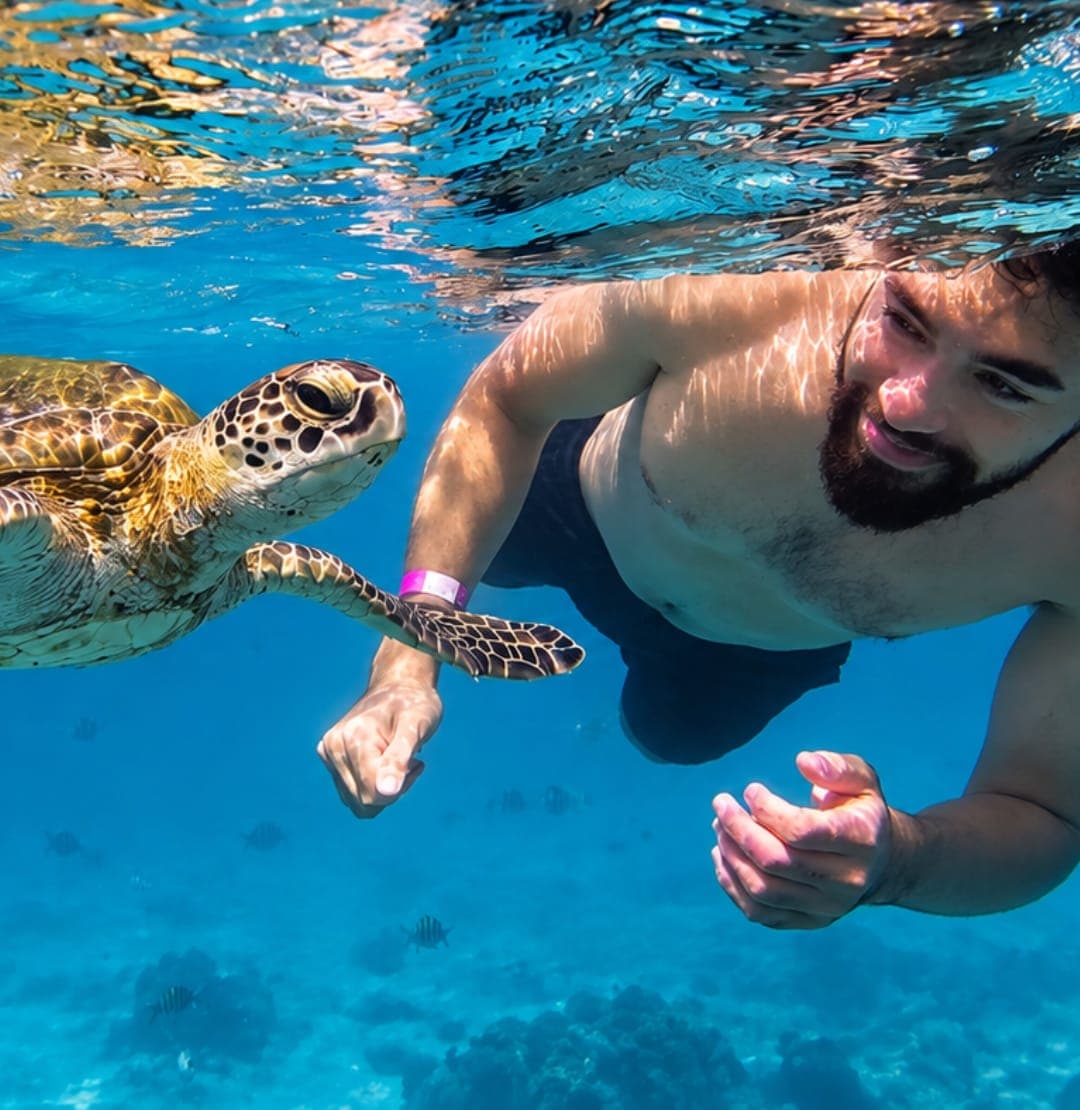 A smiling snorkeller swimming beside a green sea turtle at the Daymaniyat Islands, Oman