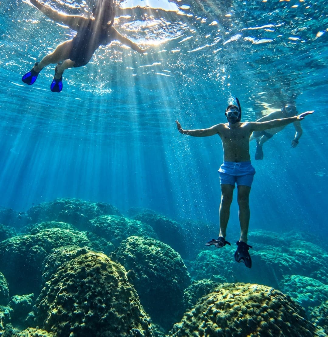Snorkellers floating in sun rays above the coral reef at the Daymaniyat Islands